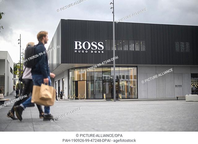 26 September 2019, Baden-Wuerttemberg, Metzingen: Visitors pass the new flagship outlet of Hugo Boss in the Outlet City. The outlet will officially open on 26...