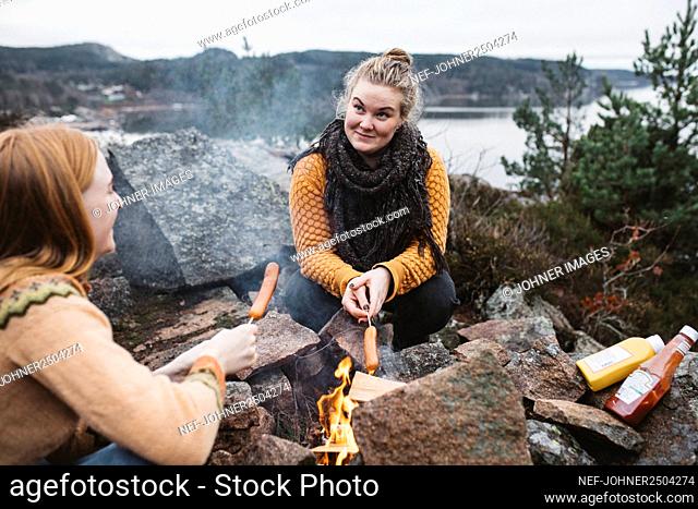 Women preparing hotdogs over campfire