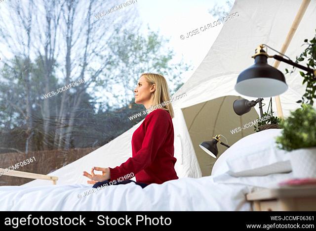 Woman doing yoga sitting on bed in transparent hotel room