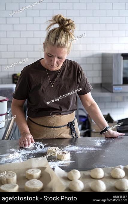 Blond woman wearing brown apron standing in a kitchen, baking danish pastries