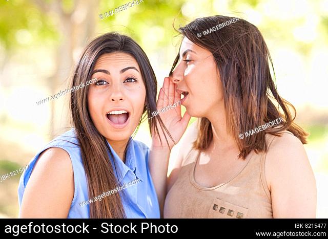 Two beautiful ethnic twin sisters whispering secrets outdoors