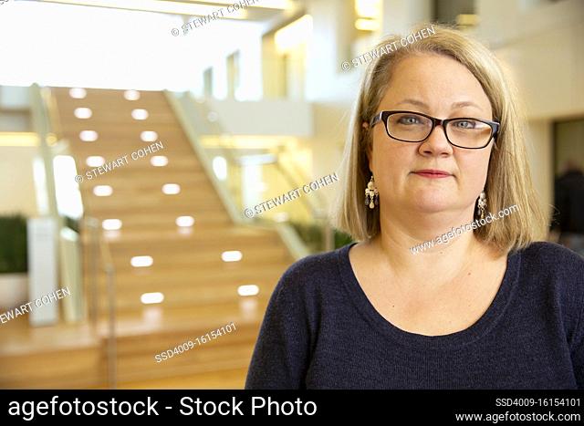 Portrait of middle aged woman wearing glasses standing by stairwell in lobby of building, smiling looking towards camera