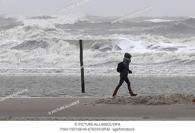 08 January 2019, Schleswig-Holstein, St.Peter-Ording: A walker walks in a storm over the North Sea beach. A storm surge is expected on the coast