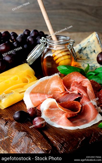 Antipasto catering platter with jerky bacon, prosciutto, salami, cheese,  and olives and grapes on a wooden background