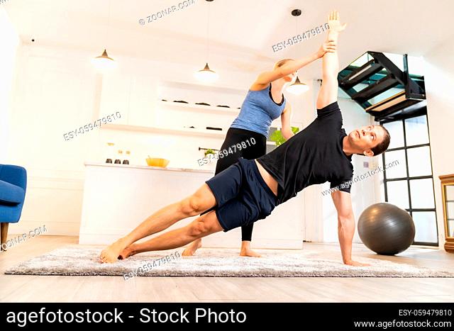 White caucasian man learning yoga at home. Female instructor or trainer coaching and adjust correct side plank pose to student