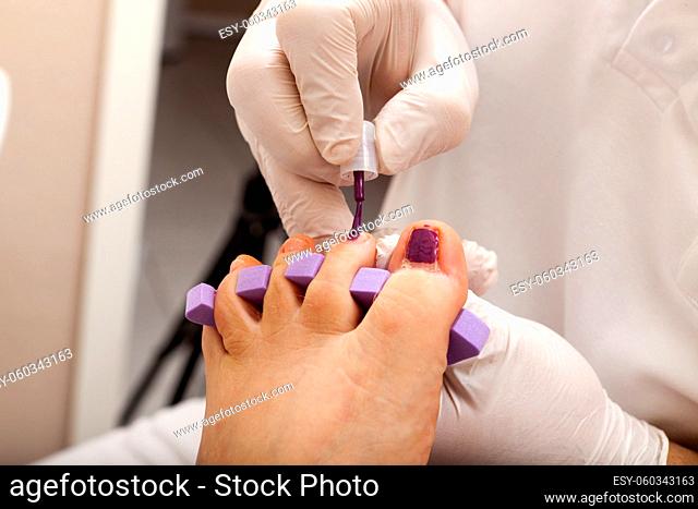 Fußpfleger lackiert Fußnägel einer Kundin
