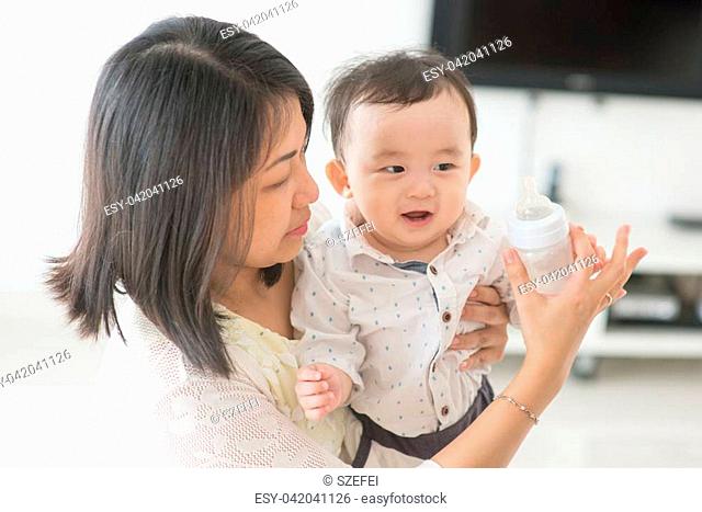 Mother holding milk bottle with 9 months old child. Asian family at home, living lifestyle indoors