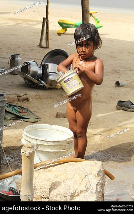 A child having a bath from a bucket outdoors. India