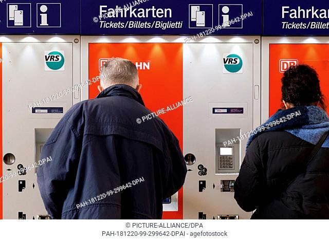 19 December 2018, North Rhine-Westphalia, Köln: Two travellers are standing in front of a ticket machine of the Verkehrsverbund Rhein-Sieg at the station...