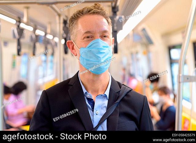 Portrait of mature businessman with mask for protection from corona virus outbreak social distancing inside the train