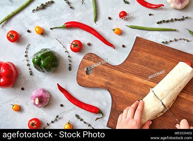 The girl cuts the finished burrito on a wooden board. Photo of a step-by-step cooking burrito. Top view, flat lay