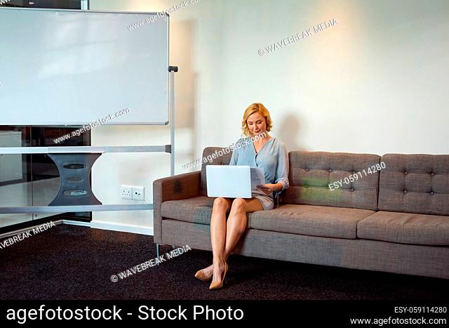 Smiling caucasian businesswoman sitting in office lounge using laptop