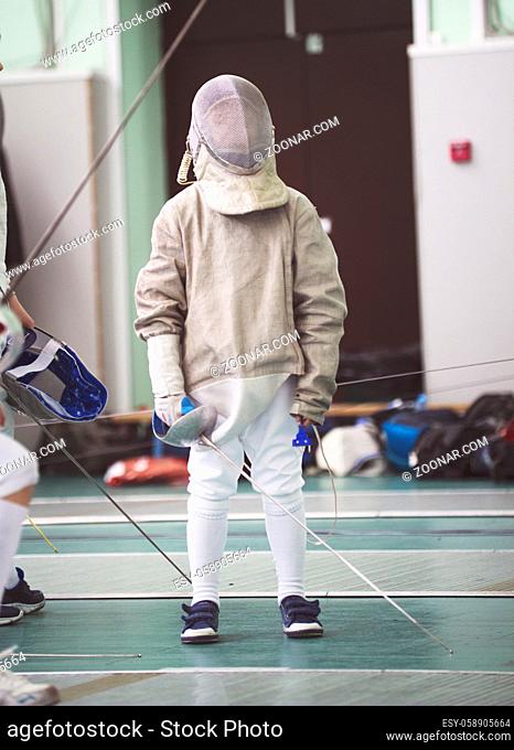Young participant of the fencing tournament in white clothes and protective mask on the fencing tournament, telephoto shot