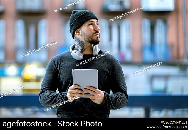 Hipster man with headphones holding digital tablet while looking away
