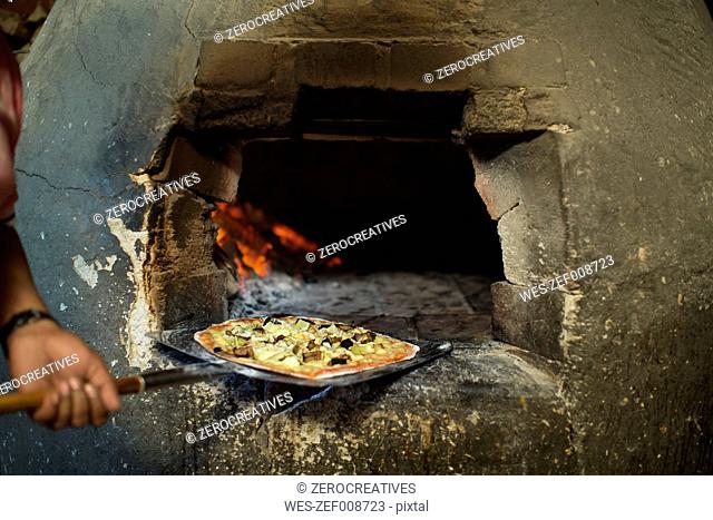 Pizza baker taking pizza out of pizza oven