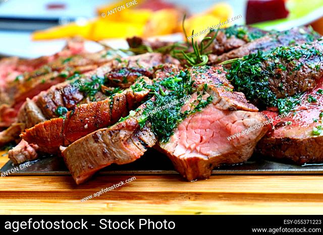 Close up big portion of sliced grill roasted beef chateaubriand tenderloin meat with thyme and herbs served on wooden cutting board, high angle view