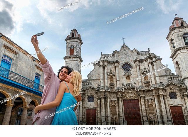 Young couple taking smartphone selfie in the Plaza de la Cathedral of Havana, Cuba