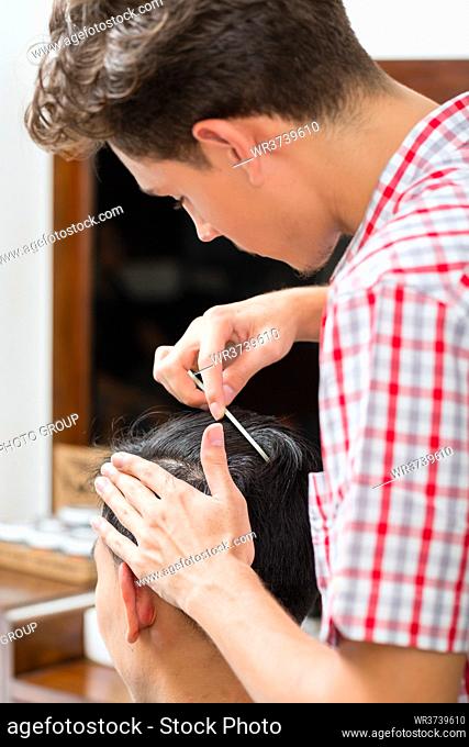 Young barber combing the customer's hair with comb in the barbershop