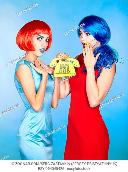 Portrait of young women in comic pop art make-up style. Females in red and blue wigs and dresses call on the phone