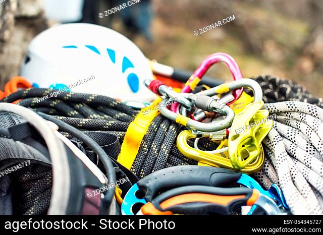 Used climbing equipment - carabiner without scratches, climbing hammer, white helmet and grey, red, green and black rope on the stone