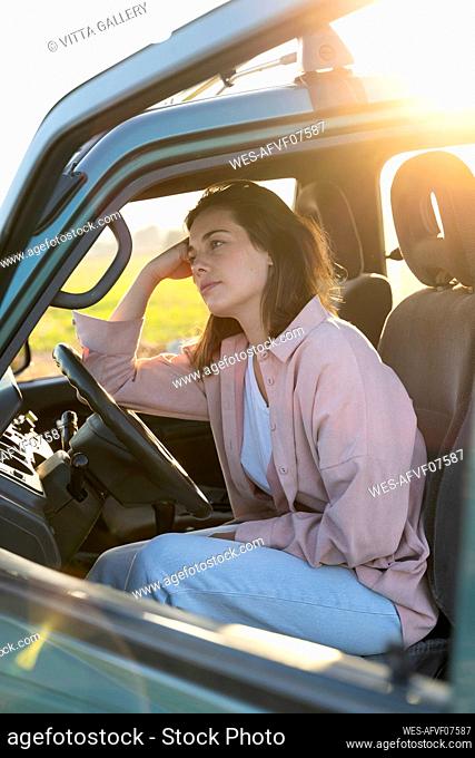 Thoughtful woman leaning on steering wheel in car during sunset
