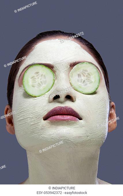 Young woman with facial mask and cucumber over her eyes