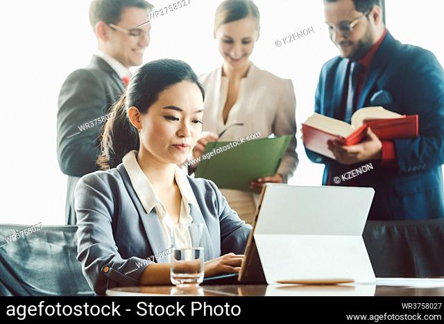 Asian business woman working on laptop with colleagues standing in background