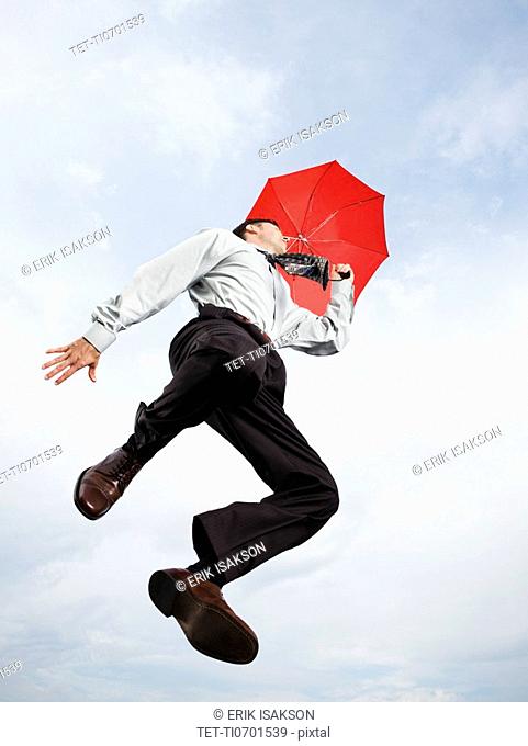 Businessman with umbrella jumping in mid-air