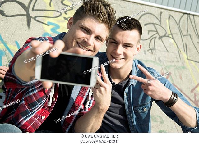 Young men in skatepark, taking self portrait photograph, using smartphone