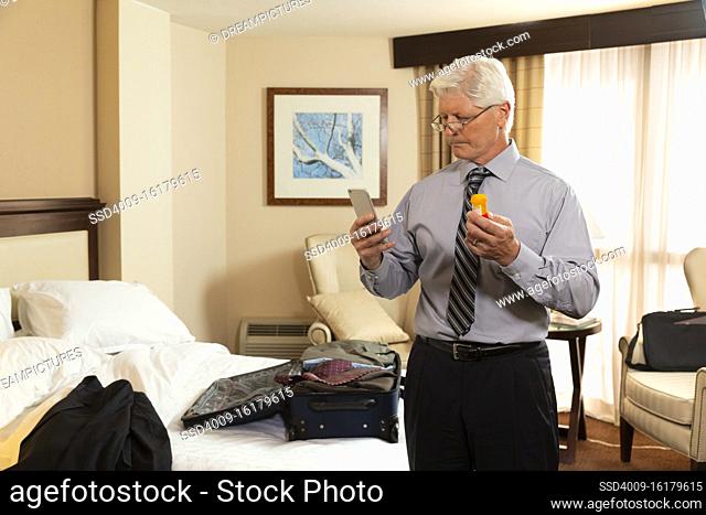 Mature Caucasian man in a hotel room, using cell phone to check prescription medication