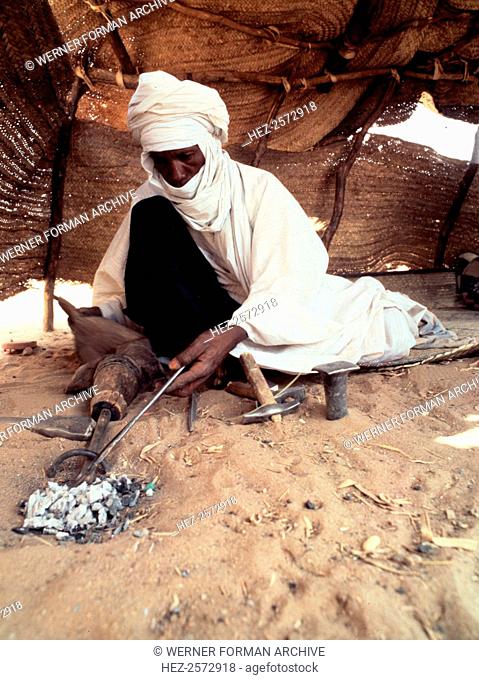 A blacksmith, possibly Tuareg or Songhay, forging iron. Country of Origin: Niger. Culture: Tuareg. Date/ Period: early 1970's