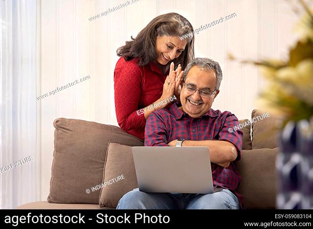 A HAPPY COUPLE SITTING TOGETHER AND USING LAPTOP FOR VIDEO CALLING