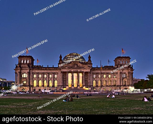 10 August 2022, Berlin: The window panes in the Reichstag building are illuminated by the light of the setting sun. (long exposure) Photo: Paul Zinken/dpa