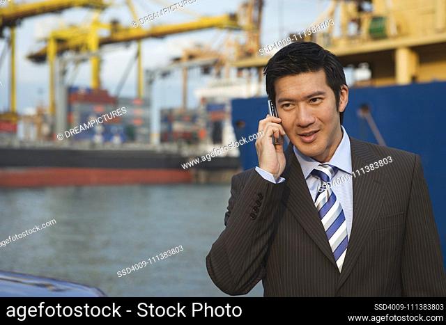 Chinese businessman talking on cell phone in shipyard