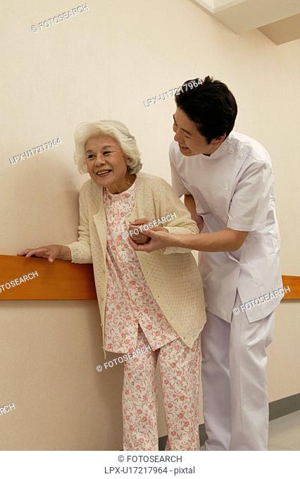 Male nurse helping senior woman walking in corridor
