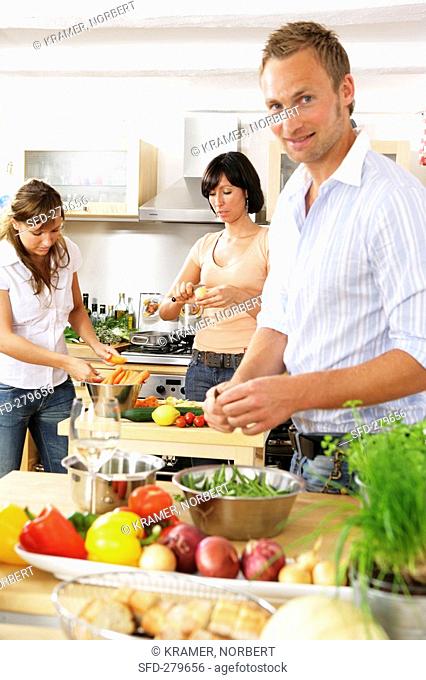 Three young people preparing vegetables in kitchen
