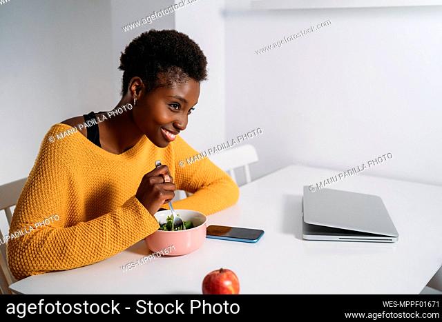 Happy young woman having healthy breakfast at table while looking away