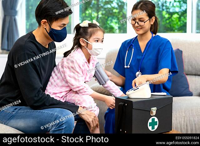 Asian doctor take blood pressure measurement to little girl child sit with her father in living room while doctor visit home