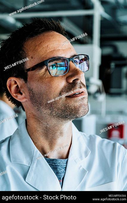 Scientist wearing eyeglasses looking away while standing with coworker in background at laboratory