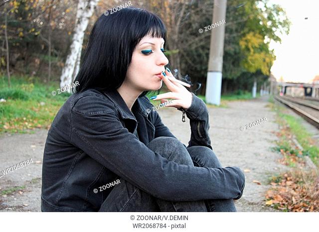 Girl sit and smoke near rails