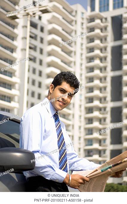 Businessman reading a newspaper beside a car, Gurgaon, Haryana, India