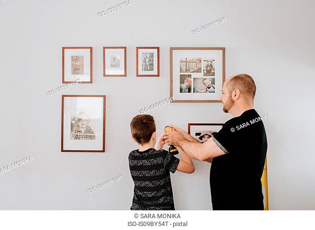 Father teaching son drill wall for picture frames