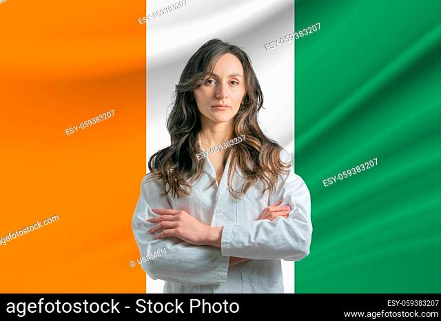 Medicine in C te d'Ivoire Happy beautiful female doctor in medical coat standing with crossed arms against the background of the flag