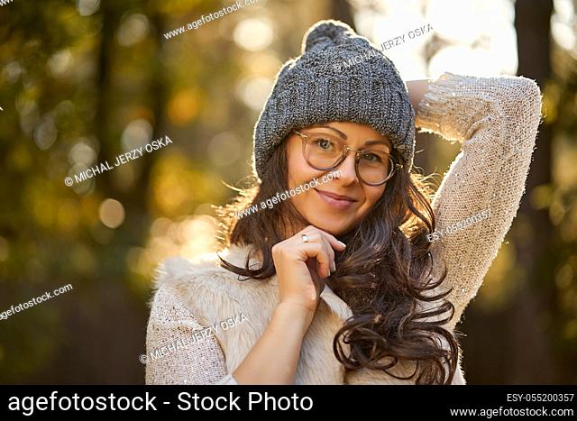 face of a beautiful woman in a cap and glasses on a background of autumn forest