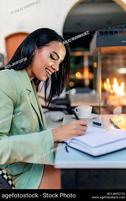 Smiling businesswoman writing in diary at cafe