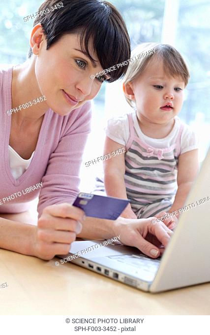 Online shopping. Mother shopping online while her 15 month old daughter watches