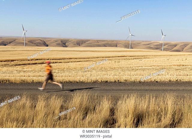 Man jogging on rural road, farmland and wind turbines in distance, Washington