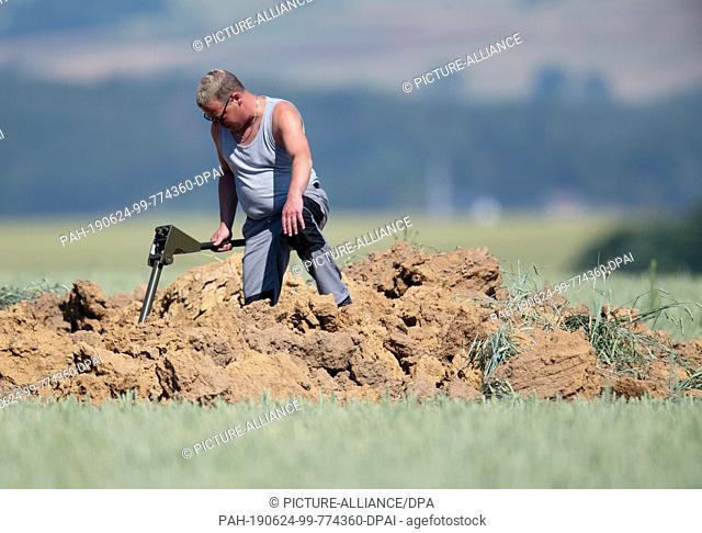 24 June 2019, Hessen, Ahlbach: Using metal probes and spades, an expert from the explosive ordnance clearance service examines a huge crater on a field