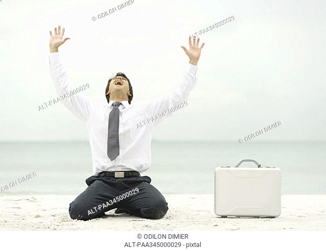 Businessman down on knees, shouting, on beach