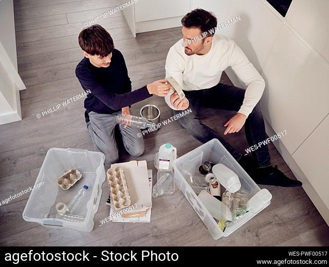 Father and son separating waste into recycling boxes